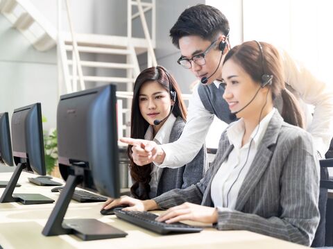 A male trainer assisting female call center employees with computers in a bright office setting