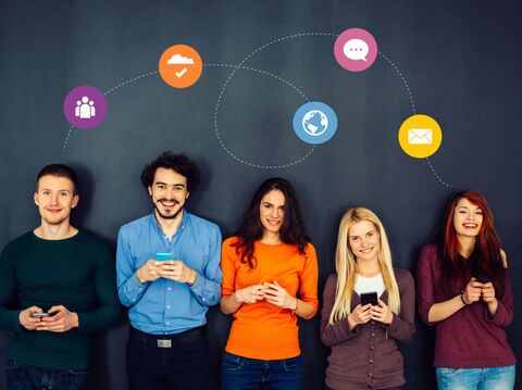 Group of five young adults, three women and two men, standing against a dark grey background, each holding smartphones and smiling. Above them are icons connected by dotted lines, representing different digital communication tools like social media, cloud storage, and email, illustrating their interconnected digital activitie