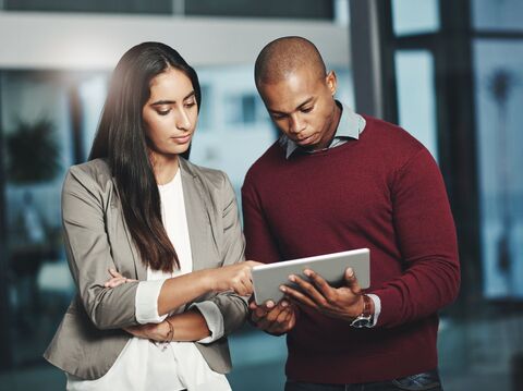 A man and woman in formal standing and watching something on a tablet