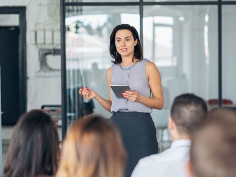 Confident woman presenting with a tablet to a group of colleagues in a modern office