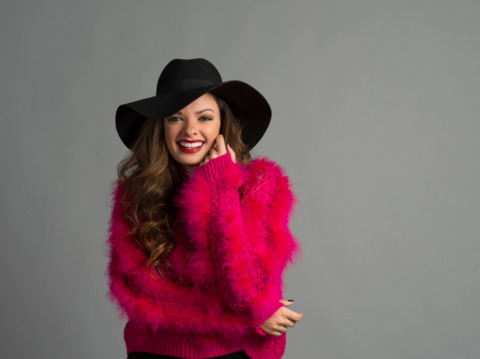 Smiling woman in a pink furry sweater and black hat posing happily