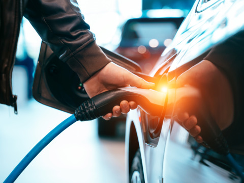 Person plugging in a charger into an electric car at a charging station