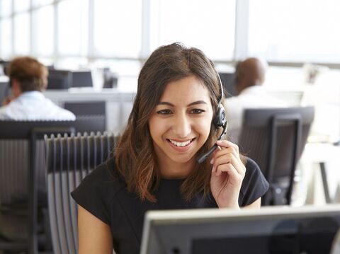 A cheerful customer service representative wearing a headset and engaging with a computer in a busy call center