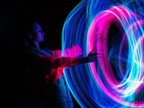 Woman in a dark room creating vibrant light painting with a pink and blue light, demonstrating artistic expression through motion