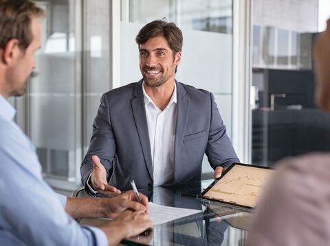 A businessman in a suit explaining charts on a tablet to colleagues during a meeting in a modern office