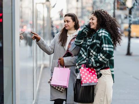 Two women shopping in the city, one pointing at something interesting