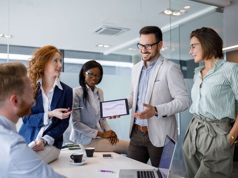 A diverse team of professionals discussing data on a tablet in a modern office