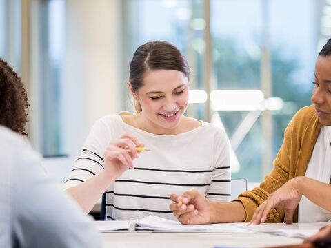 Three colleagues, one smiling, collaborating over documents in a bright office