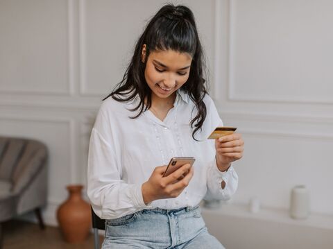 Young woman in a white blouse using a smartphone and credit card to shop online