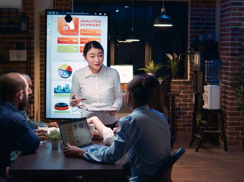 A woman presenting analytics on a digital screen to colleagues in a dimly lit, stylish office