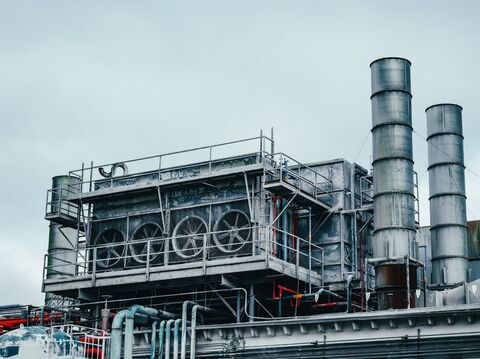 A picture of an industrial complex with tall smokestacks and storage tanks. The sky is hazy and gray.