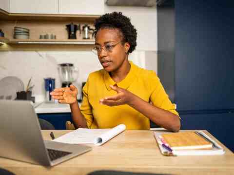 A woman in a yellow dress discussing project details with colleagues in a casual, modern kitchen setting