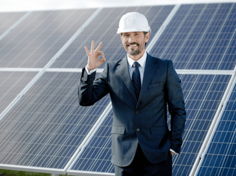 Engineer in hard hat giving a victory sign in front of solar panels