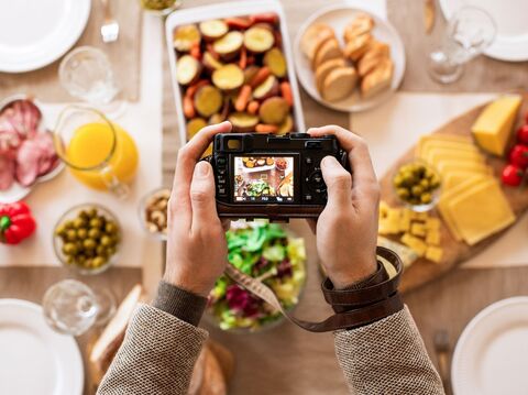 Hands holding a camera capturing a variety of foods arranged on a table