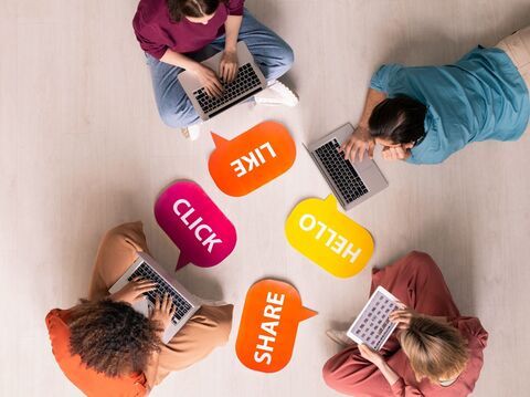 In a room, four people were sitting and lying on the floor, forming a circle. They are all using laptops and tabs. There are likes, hellos, shares, and clicks kept between circle