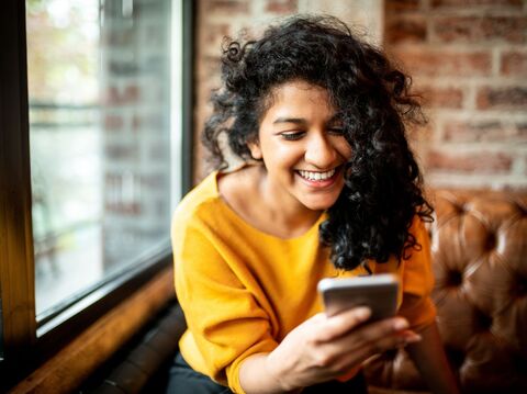 A woman in a yellow t-shirt is sitting on a sofa and watching her phone