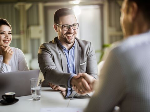 Two business professionals, a man and a woman, smiling and shaking hands in a bright office