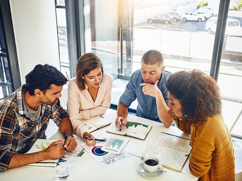 Diverse group of four professionals discussing financial charts and data in a modern office