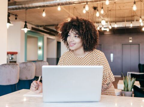 Curly-haired woman smiling and using a laptop in a cafe, holding a credit card