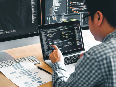 A male developer reviewing codes on multiple screens in a tech office setup