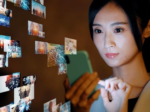 Young woman using smartphone to interact with a digital wall of connected photos and virtual interfaces