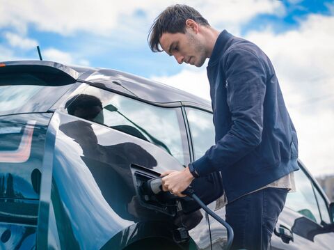 A man charging an electric car in the open sky