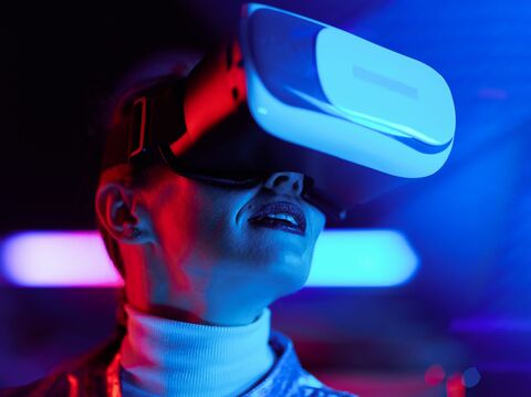 A young woman wearing a virtual reality headset illuminated by neon blue and red lights, expressing awe and excitement