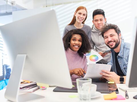 A cheerful group of young professionals gathered around a computer, discussing color palettes and design options