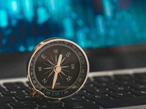 Close-up of a vintage compass on a keyboard, symbolizing navigation in the digital world with blue data visuals in the background