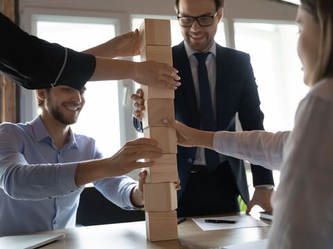 A few people in an office cabin are arranging some wooden bricks like a tower with smiley faces