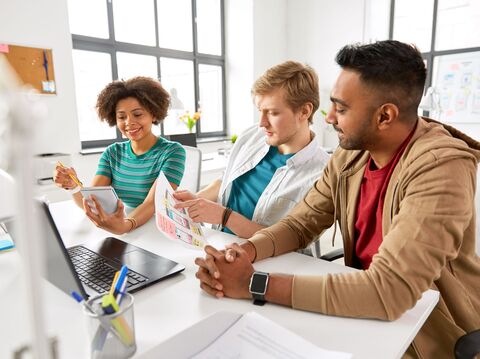 In an office room, three people were sitting on a chair near a desk and looking at some data on paper