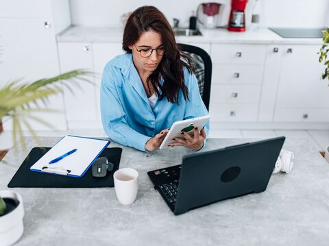 A woman in glasses working at a desk with a laptop and tablet, concentrating on her tasks