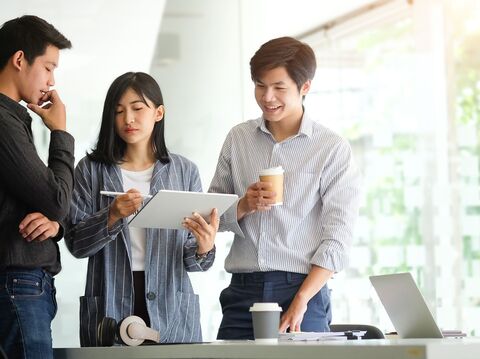 A group of three people are standing and having a discussion near a desk