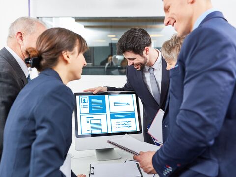 A diverse group of professionals, including men and women in business attire, enthusiastically discussing over a digital interactive display showing various document and graph icons in a modern office setting