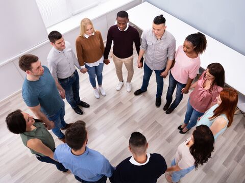 A diverse group of people standing in a circle holding hands, viewed from above