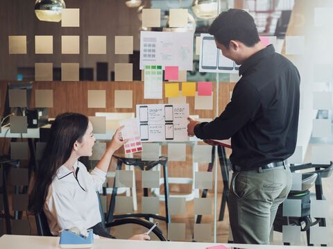 Two colleagues discussing mobile app design, with design sketches on a glass wall