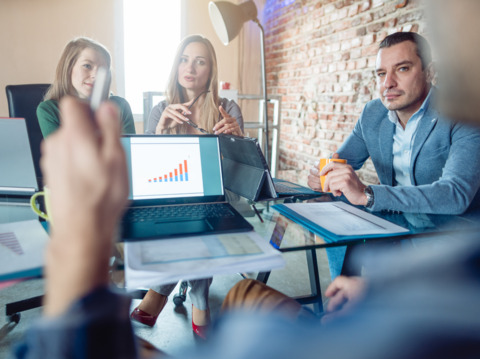 A group of professionals in a meeting, discussing a chart on a laptop screen