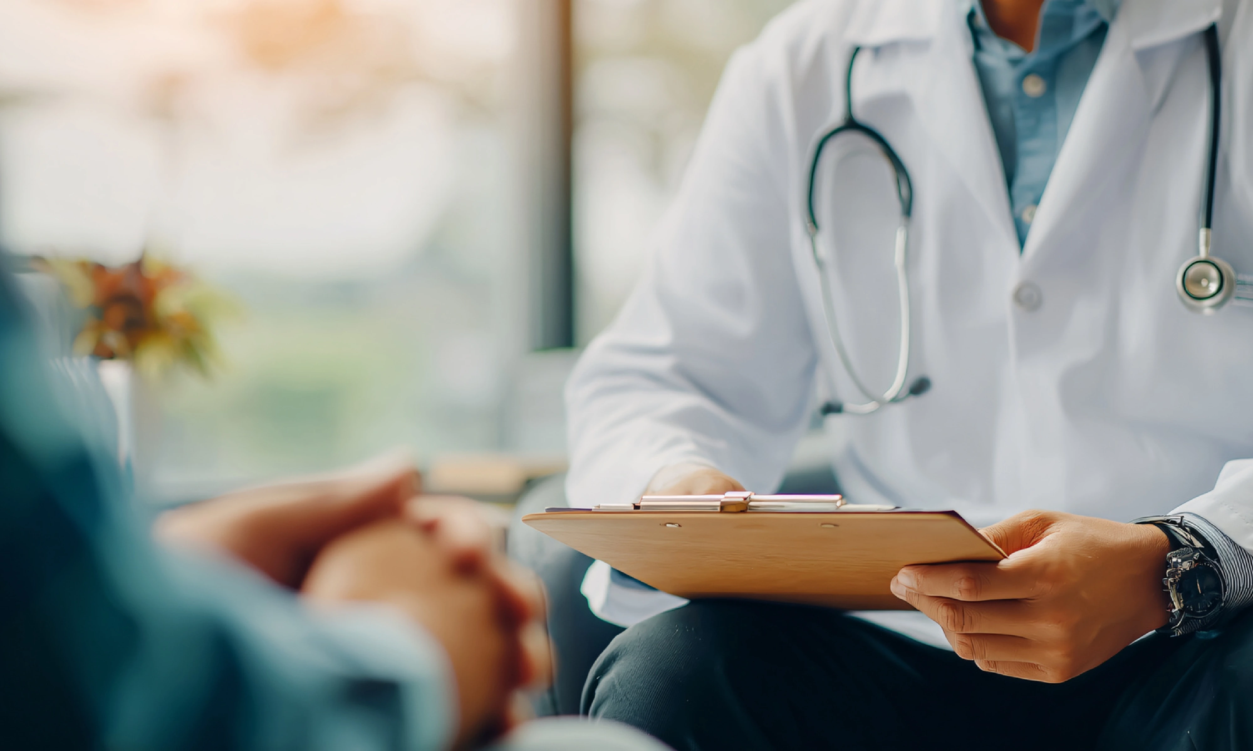 A doctor in a white coat holding a clipboard while consulting a patient in a clinic setting, representing ongoing subscription-based healthcare and continuous patient engagement.