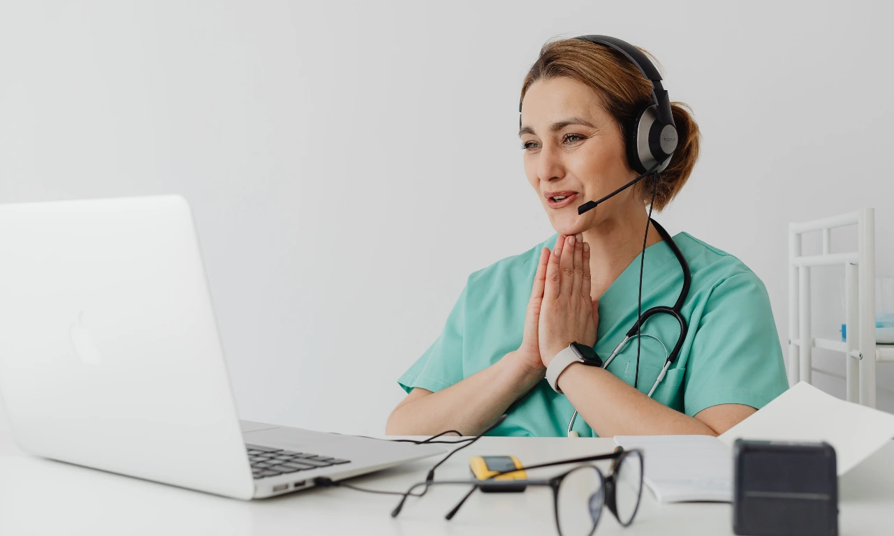 Female healthcare professional with a headset conducting a virtual consultation on a laptop, representing telehealth and digital care services.