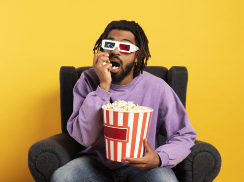 Man in purple sweater watching 3D movie and eating popcorn