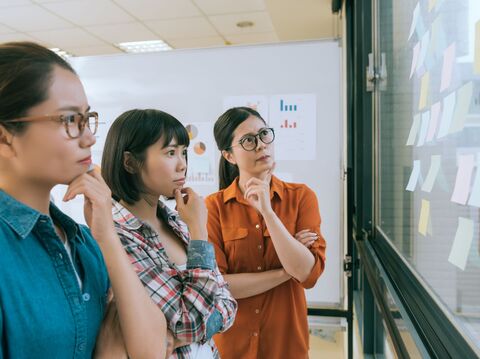 Three young women discussing something while looking at a whiteboard with charts and data visualizations