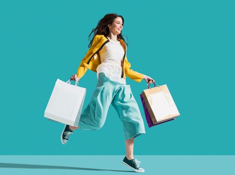 A woman with shopping bags in both her hands frolicking around with a matt cyan background