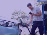 A man charging an electric vehicle at a public charging station while looking at his smartphone