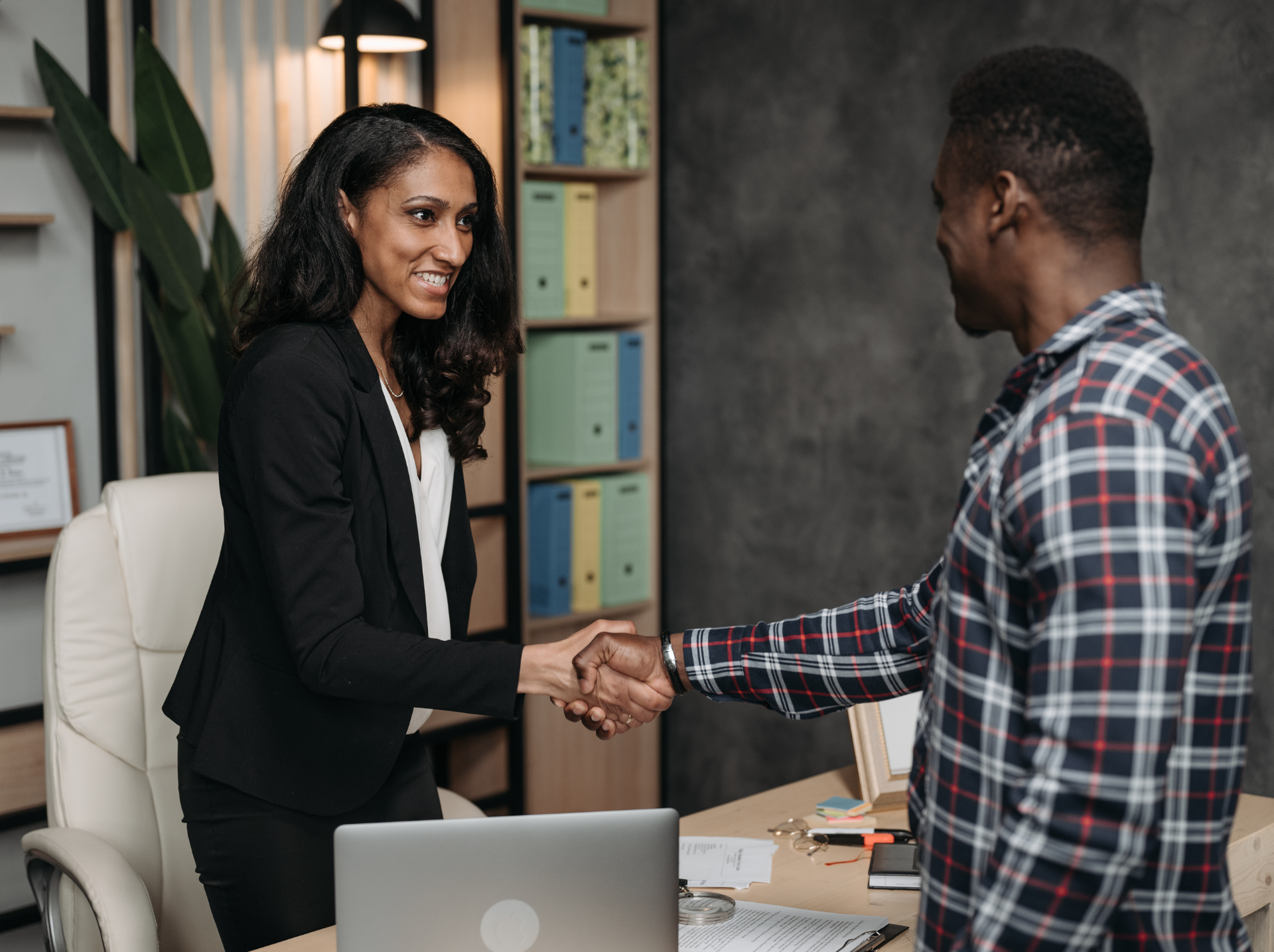  A man and woman shaking hands over a desk, symbolizing agreement and collaboration in a professional setting.